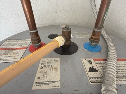 Photo looking down at a water heater: copper supply lines, the relief valve, and the equipment labels on the tank top.